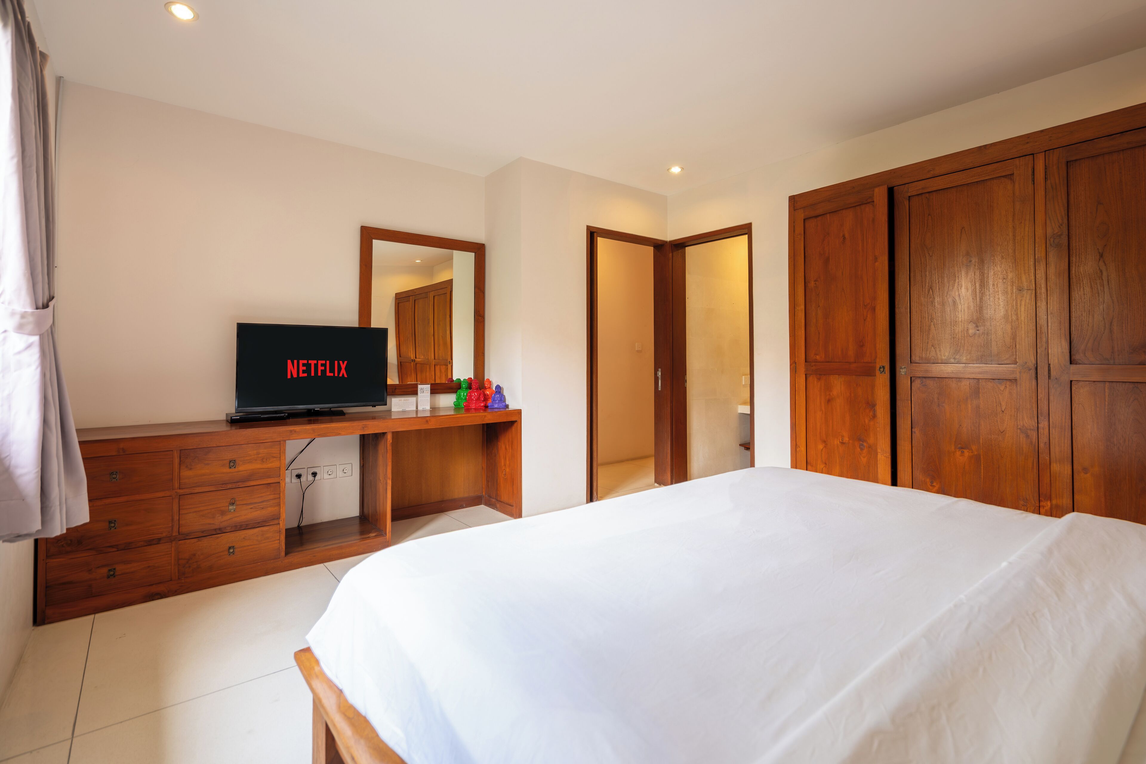Un dormitorio con cama, cómoda de madera, televisor y espejo.