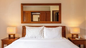 Una cama bien hecha con sábanas blancas, flanqueada por dos mesitas de noche con lámparas, y un espejo grande sobre la cama.