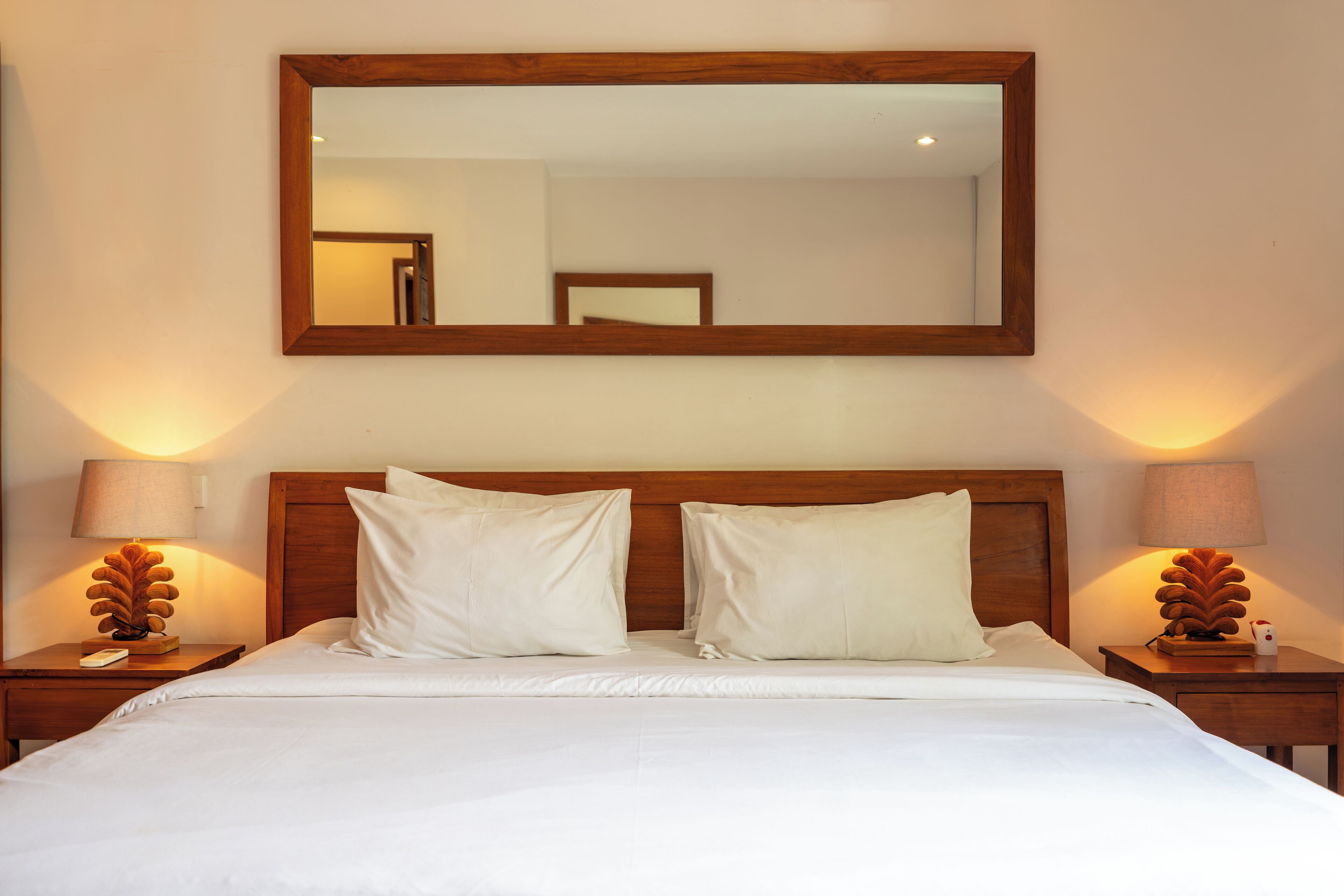 Una cama bien tendida con dos almohadas, un cabecero de madera y dos mesitas de noche con lámparas.