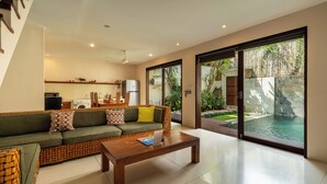 Una sala de estar moderna con un sofá verde, una mesa de centro de madera y un amplio ventanal corredero que da a una piscina.