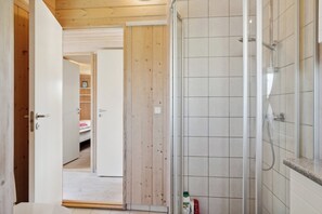Ein Badezimmer mit Dusche, einer Holztür und einem gefliesten Boden.