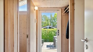 Een houten deur die leidt naar een terras met een bank, een metalen hekwerk en uitzicht op een huis en groen.