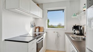 Una cocina compacta con armarios blancos, encimera negra, ventana con vistas y un lavamanos.