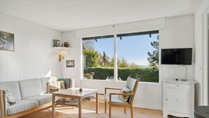 Una habitación con sofá, sillón, mesa, televisor y ventana con vista a zonas verdes.