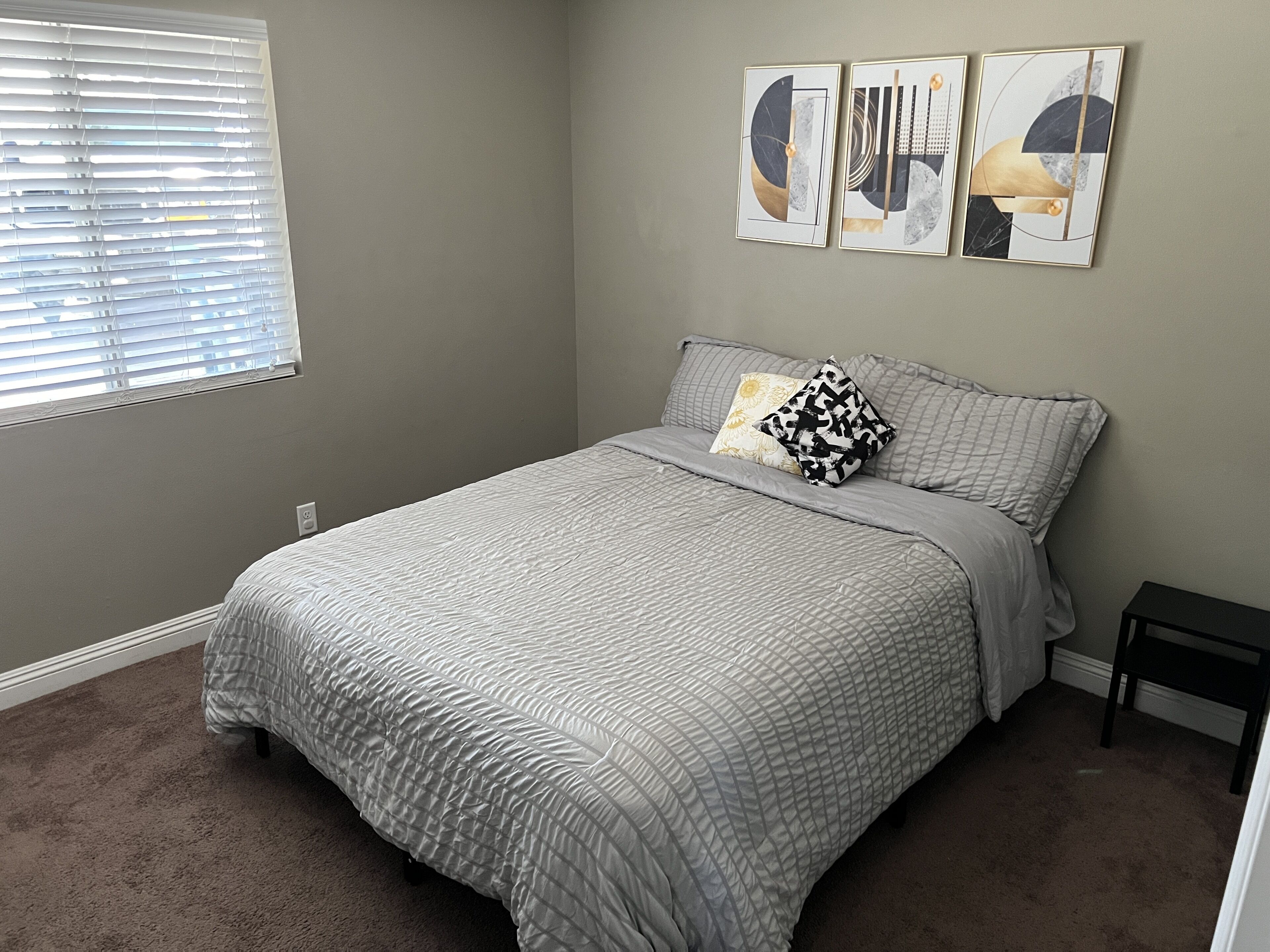 A bedroom with a bed, a window with blinds, and three wall art pieces.