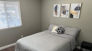 A bedroom with a bed, a window with blinds, and three wall art pieces.