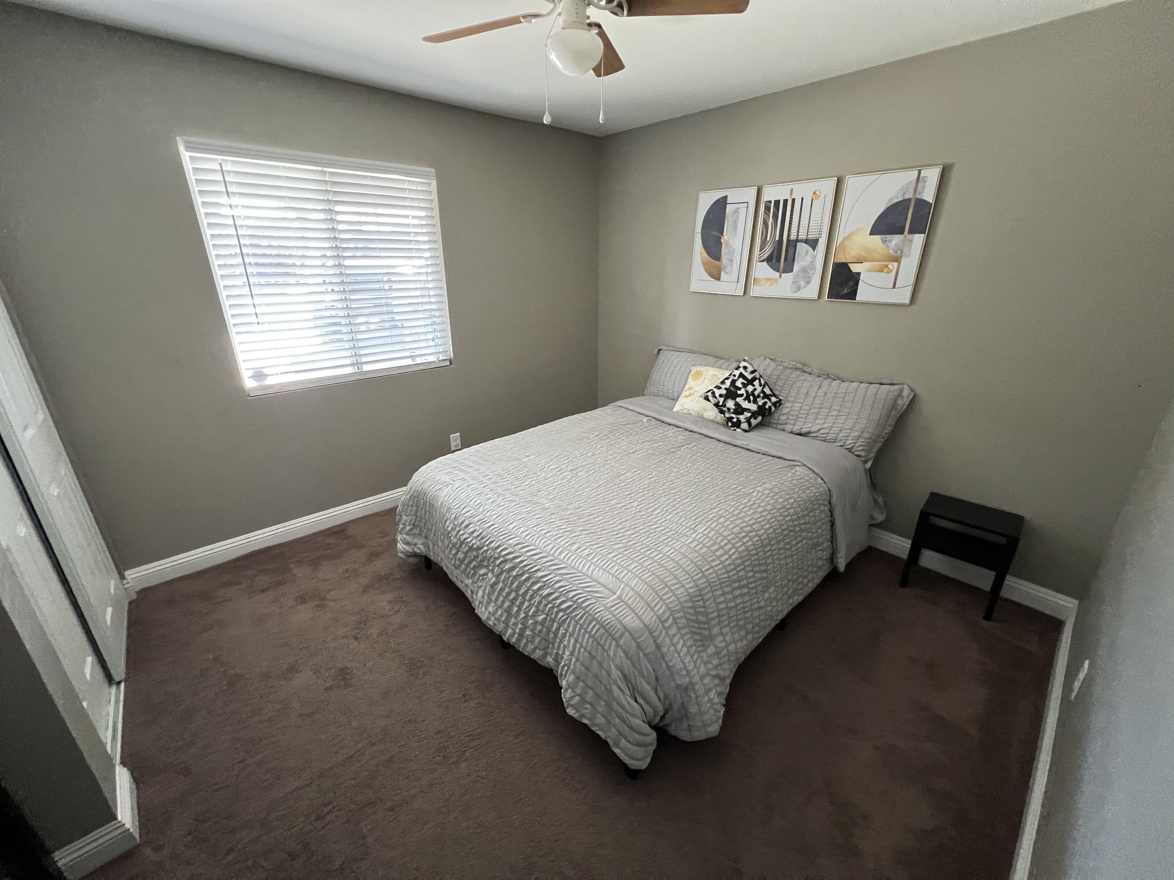A bedroom with a bed, a ceiling fan, a window with blinds, and wall art.