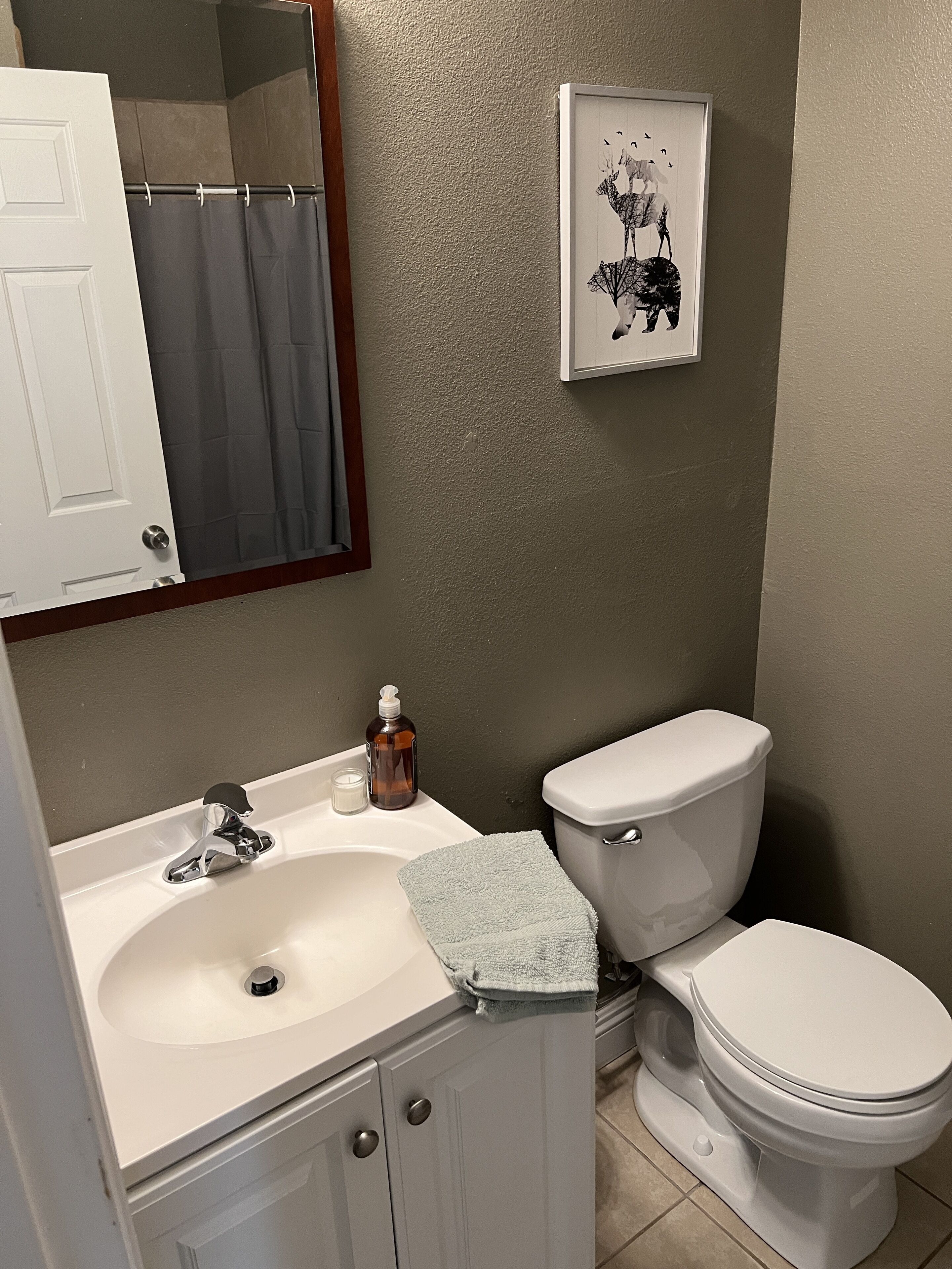 Un baño con lavamanos blanco, inodoro, un cuadro en la pared y cortina de ducha.