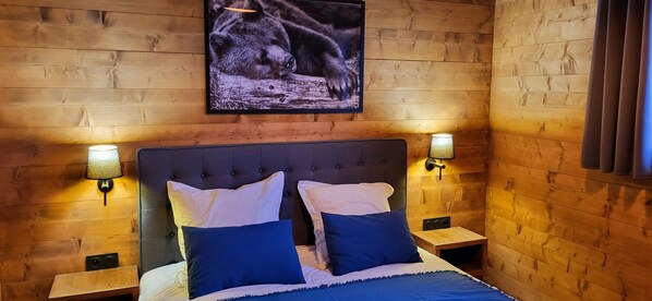 A wooden-paneled room with a bed, two bedside lamps, and a framed picture on the wall.