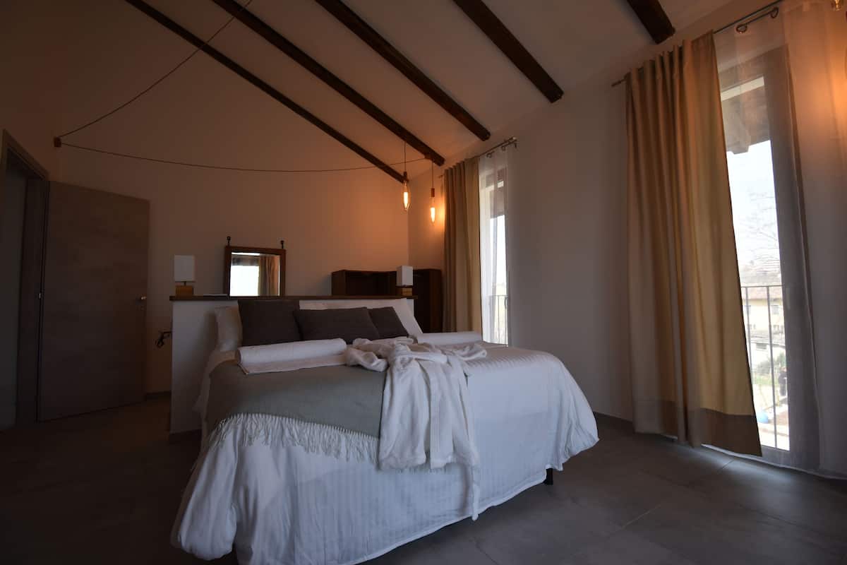 Une chambre à coucher avec un grand lit, une table de chevet, un miroir et une fenêtre avec des rideaux.