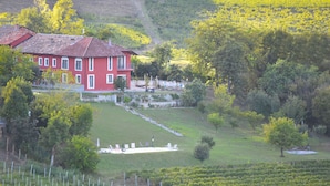 Ein rotes Gebäude mit geneigtem Dach, umgeben von einem gepflegten Rasen und einem Weinberg.