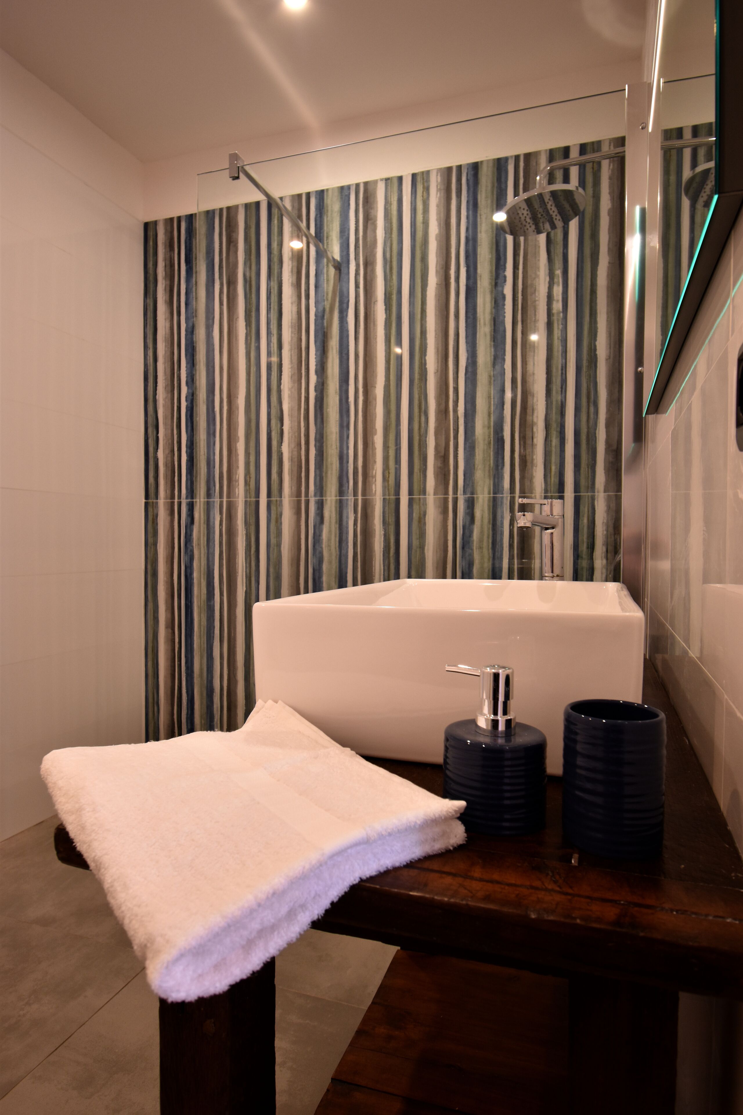 Ein modernes Badezimmer mit einer großen Badewanne, einer Duschkabine aus Glas und einer hölzernen Sitzbank mit Handtuch.
