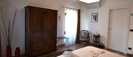 Habitación de hotel con un armario de madera grande, una cama con toallas, una silla, una mesita con una botella y un cuadro en la pared.