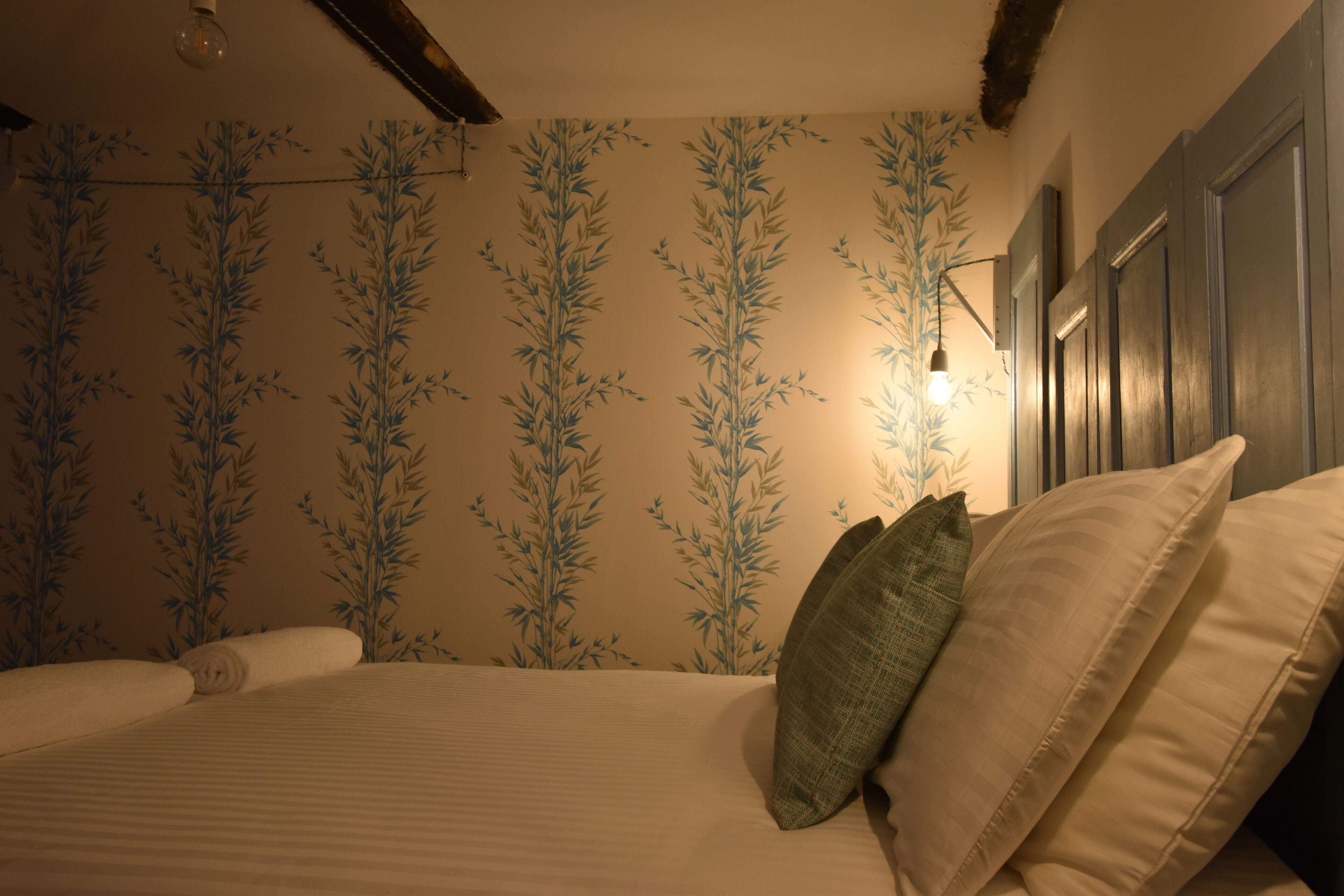 Een slaapkamer met een bed, kussens, een wand met een bamboepatroon en een hanglamp.