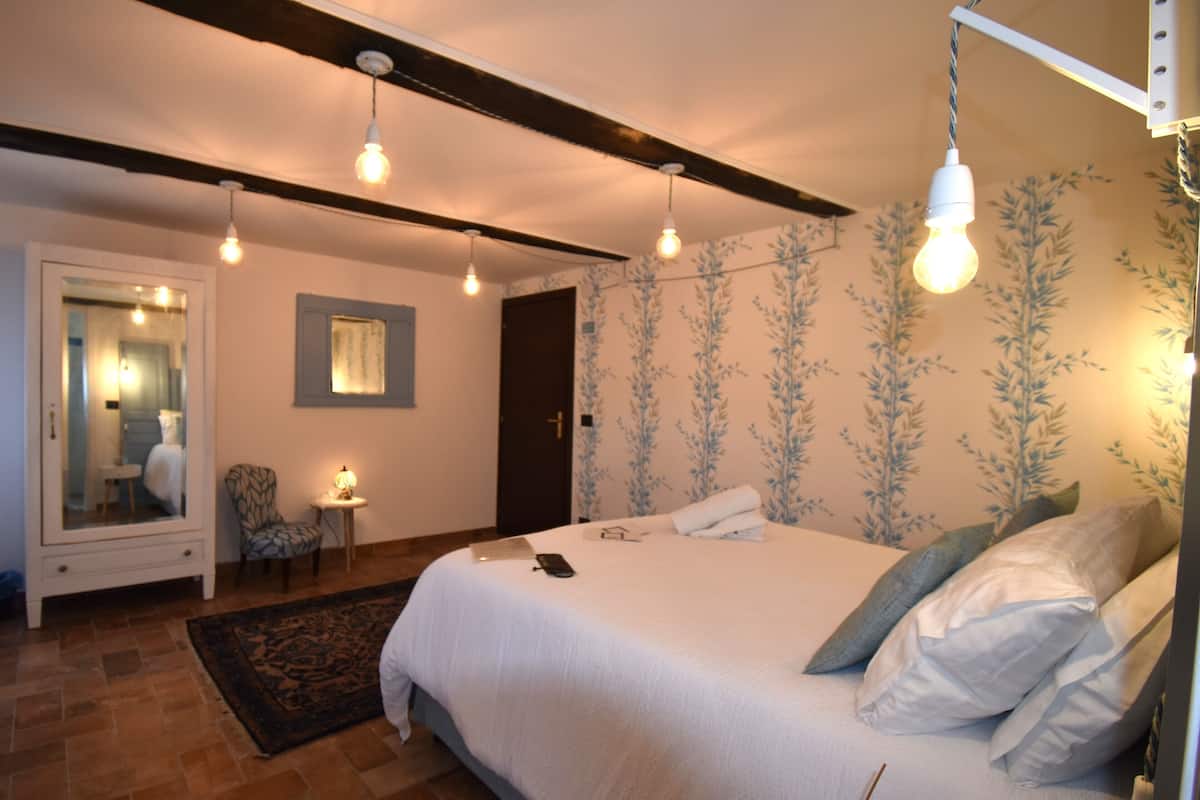 Une chambre à coucher avec un grand lit, une table de chevet, une chaise, un miroir et une porte.