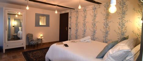 A bedroom with a large bed, a bedside table, a chair, a mirror, and a door.