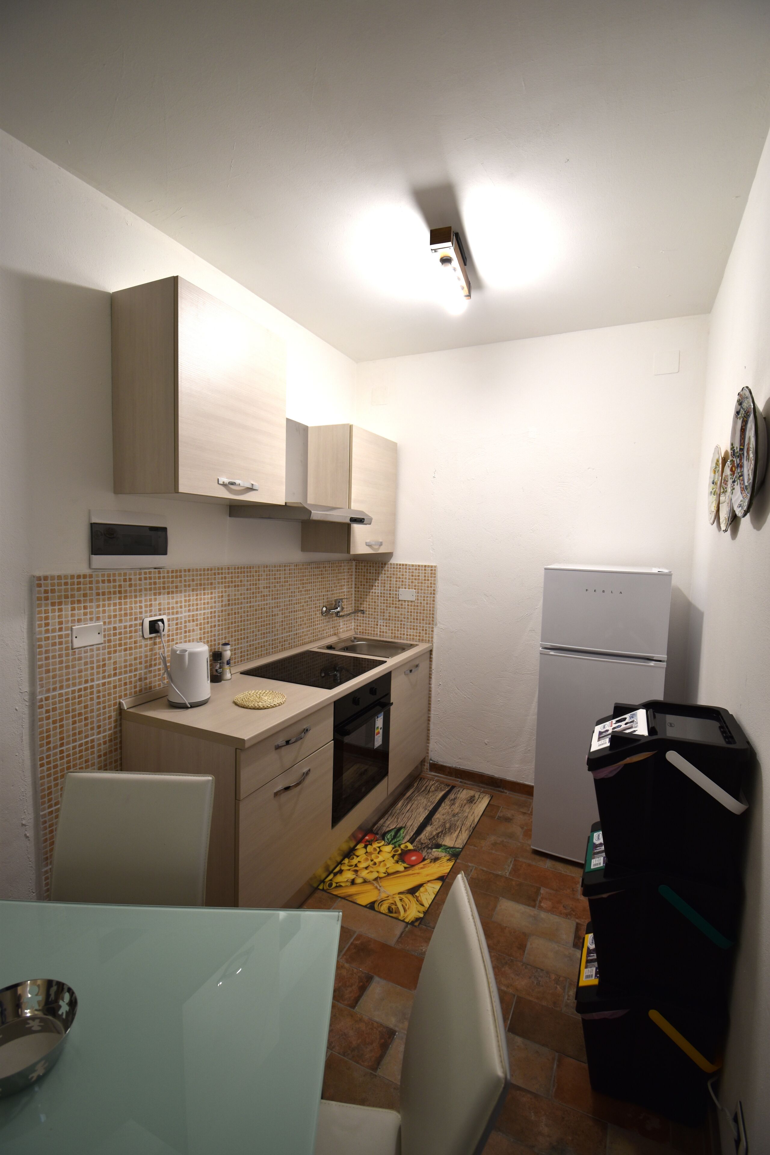 Cocina compacta con microondas, pileta y refrigerador. Hay una mesa de comedor con sillas y un alfombra estampado en el piso.