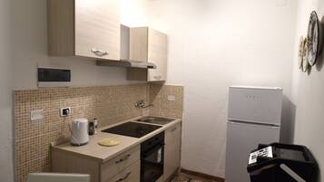 Cocina compacta con microondas, pileta y refrigerador. Hay una mesa de comedor con sillas y un alfombra estampado en el piso.