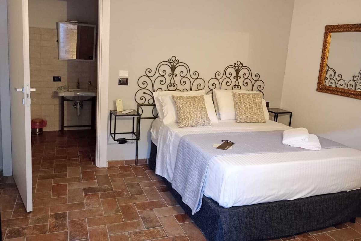 Une chambre à coucher comprenant un lit, une table de chevet, une commode, un miroir et une salle de bain visible à travers une porte ouverte.