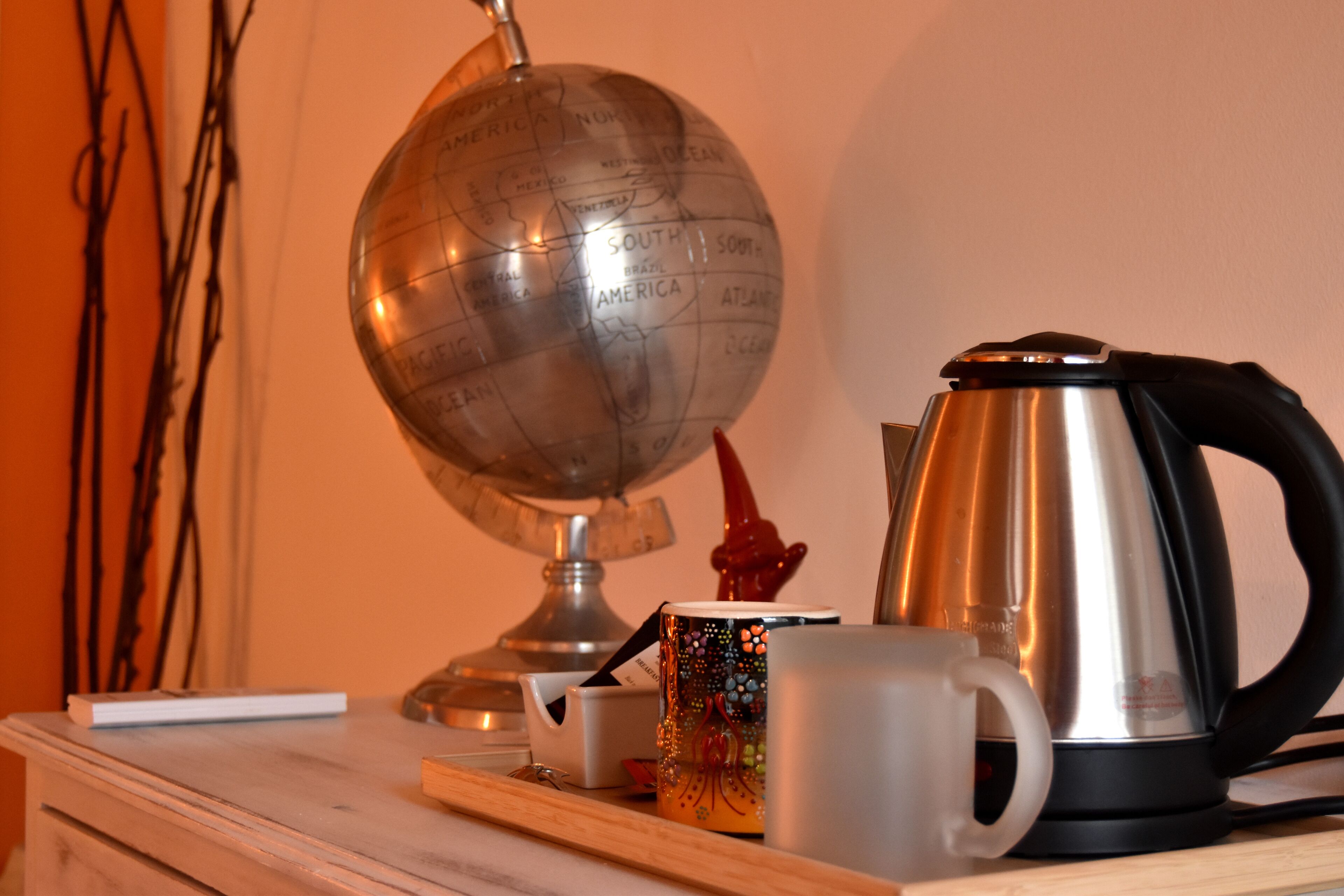 A globe, a kettle, and two mugs on a wooden shelf.