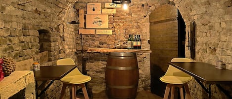Un sótano con paredes de ladrillo, barriles de madera y mesas con sillas amarillas.