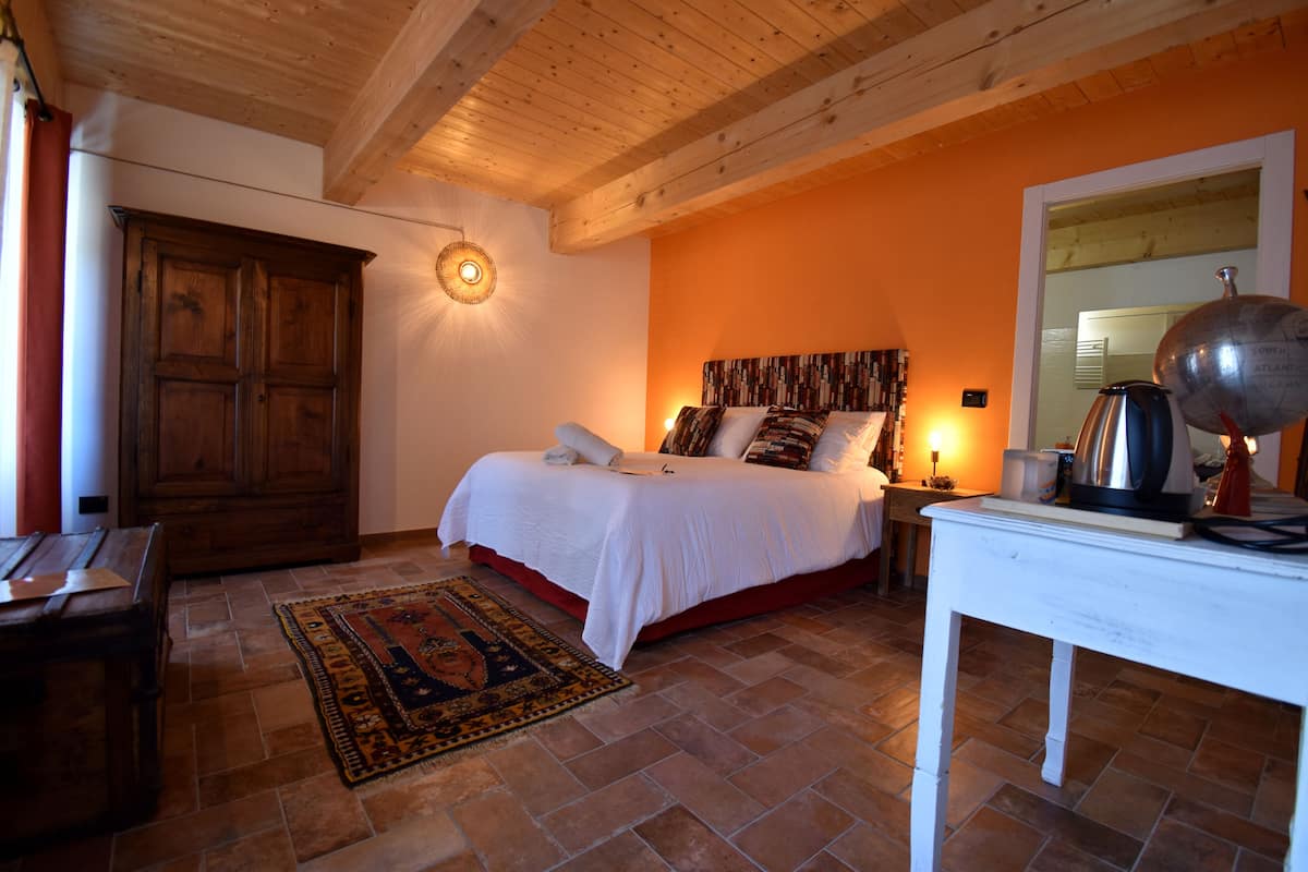 Une chambre avec un plafond en bois, un lit doté d’une tête de lit à motifs, une table de chevet avec une lampe et un tapis rouge.