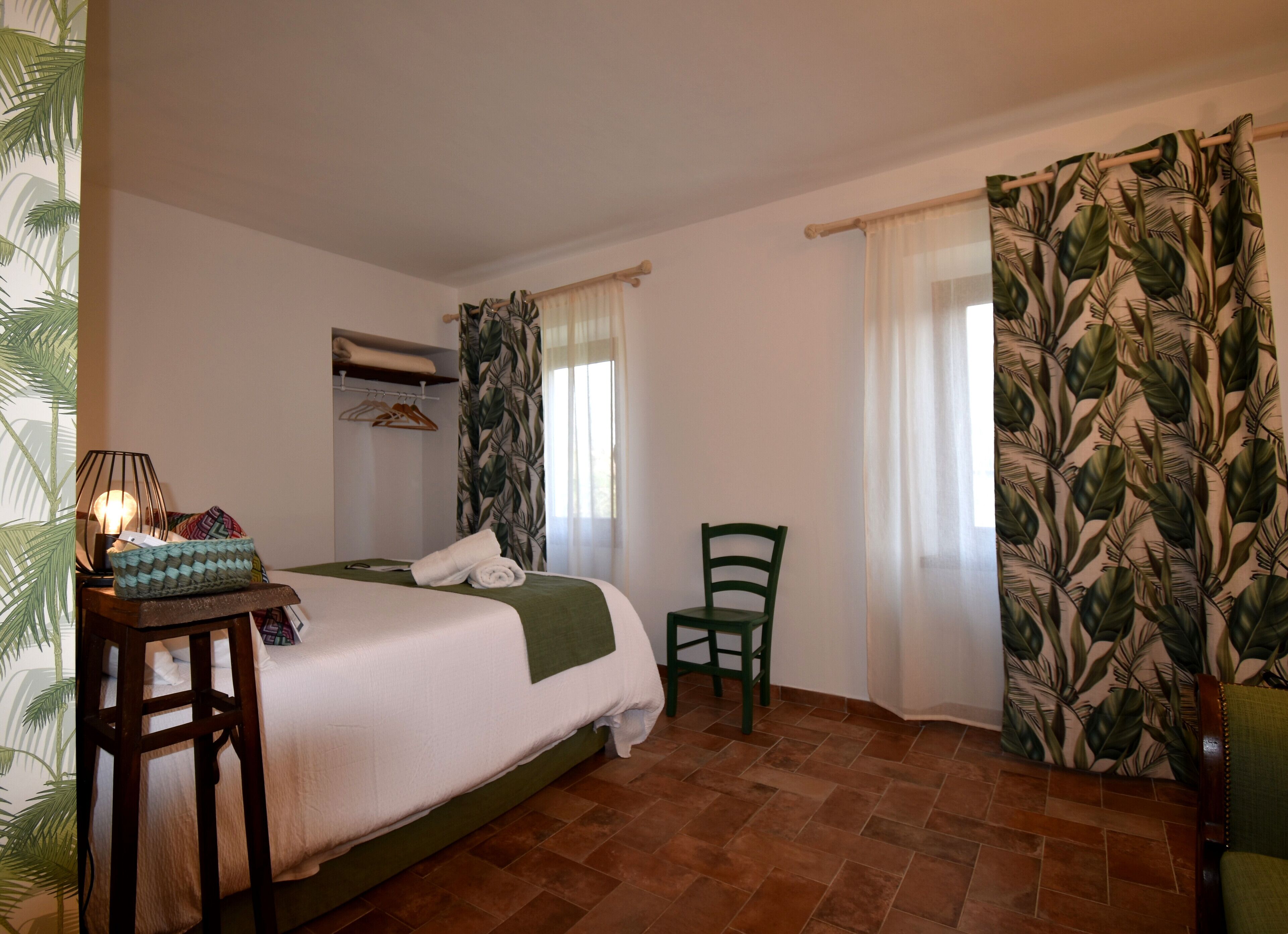 A neatly arranged bedroom with a bed, a chair, a table with a lamp, and a wardrobe.