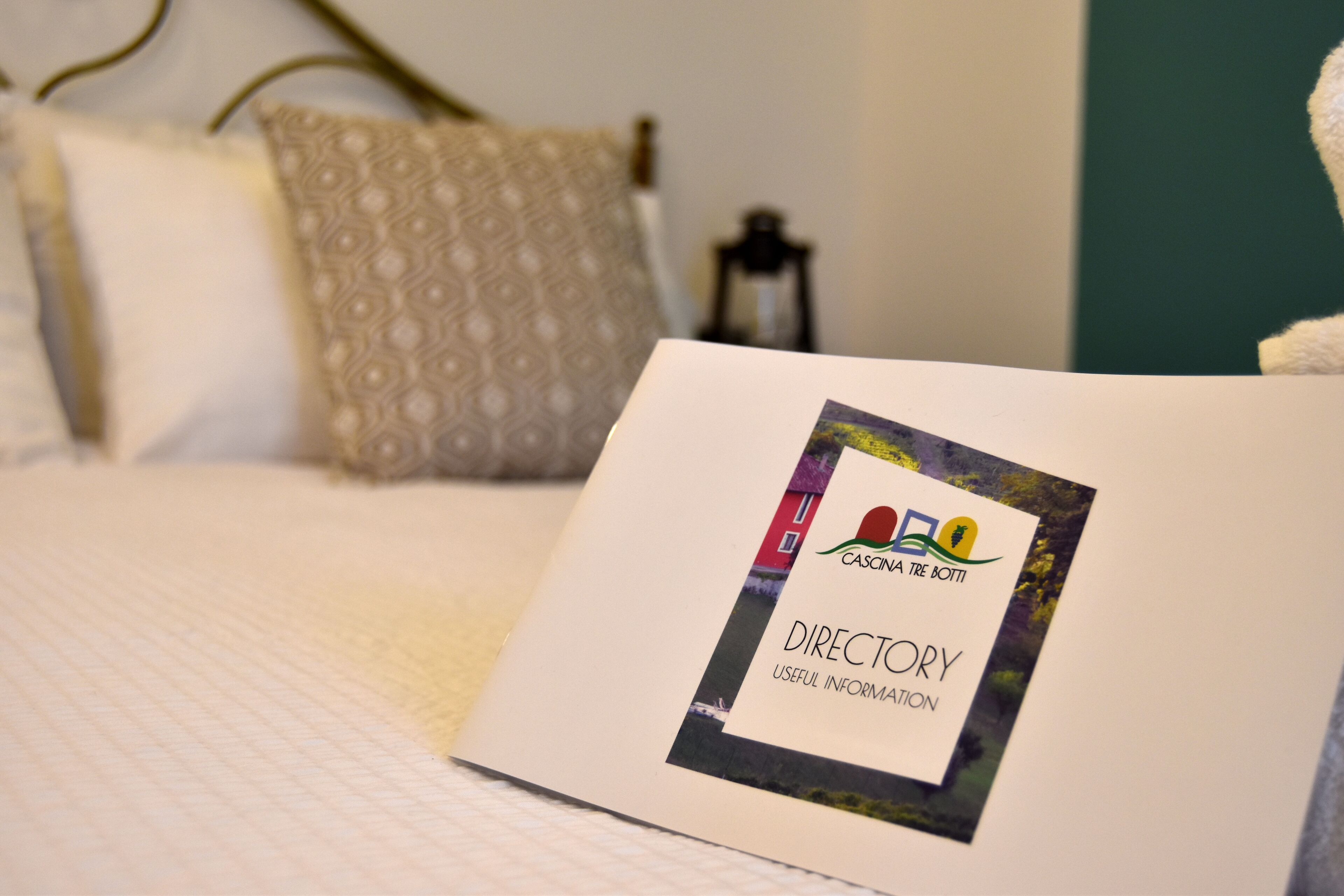 Um folheto com o título 'DIRECTORY USEFUL INFORMATION' sobre uma cama com almofada estampada e um candeeiro no fundo.