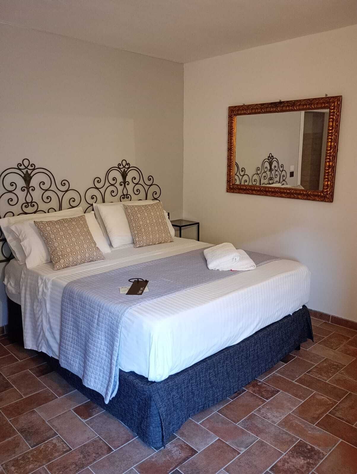 Un lit bien fait, avec une tête de lit à motifs, une table de chevet et un miroir au mur.
