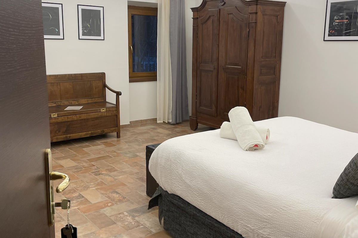 Une chambre d’hôtel avec un lit, une armoire en bois, un banc en bois, une petite table et une porte dotée d’un trou de serrure.