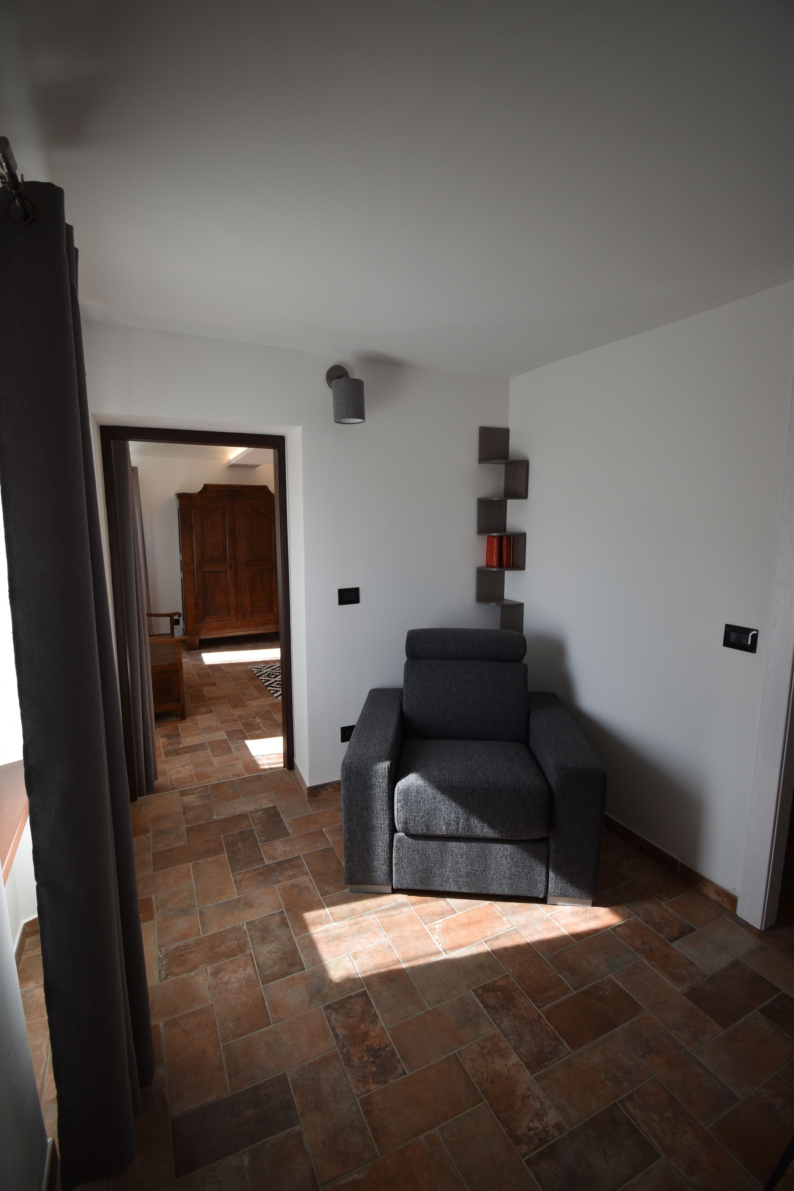 Une pièce avec un canapé gris, une armoire en bois et un sol carrelé.