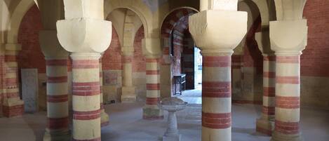 A historical building with striped columns and arches, a stone floor, and a mosaic on the wall.