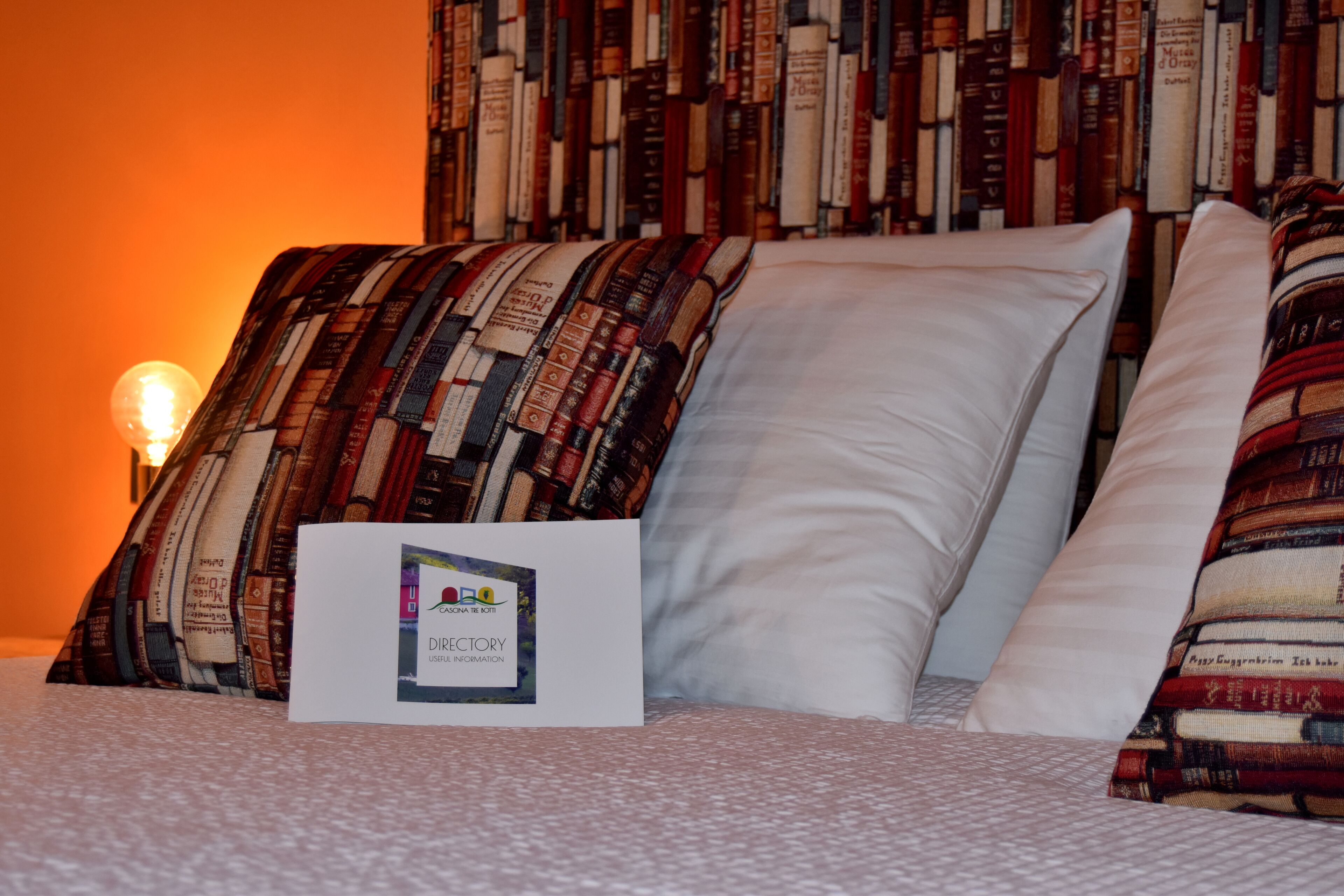 A neatly made bed with a patterned pillow and a white pillow, a sign with 'DIRECTORY' and 'USER INFORMATION' text, and a wall of books behind.