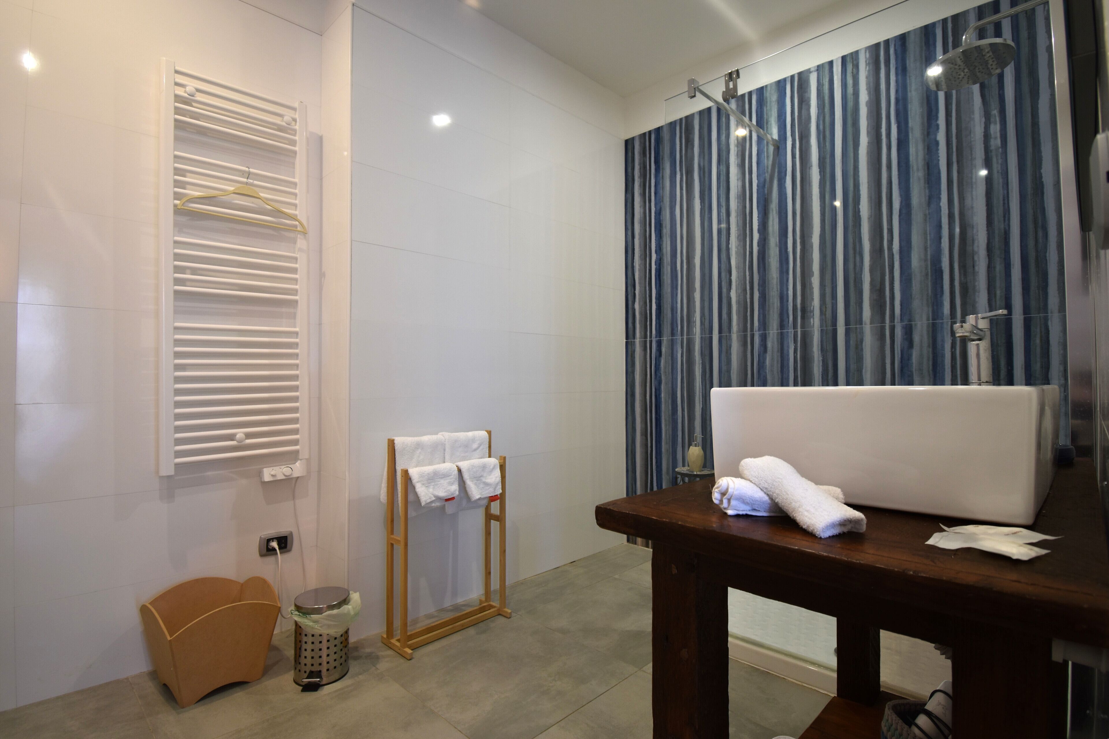 Une salle de bain moderne avec un grand miroir, une table en bois avec des serviettes, un porte-serviettes et un espace douche avec un mur à rayures bleues.