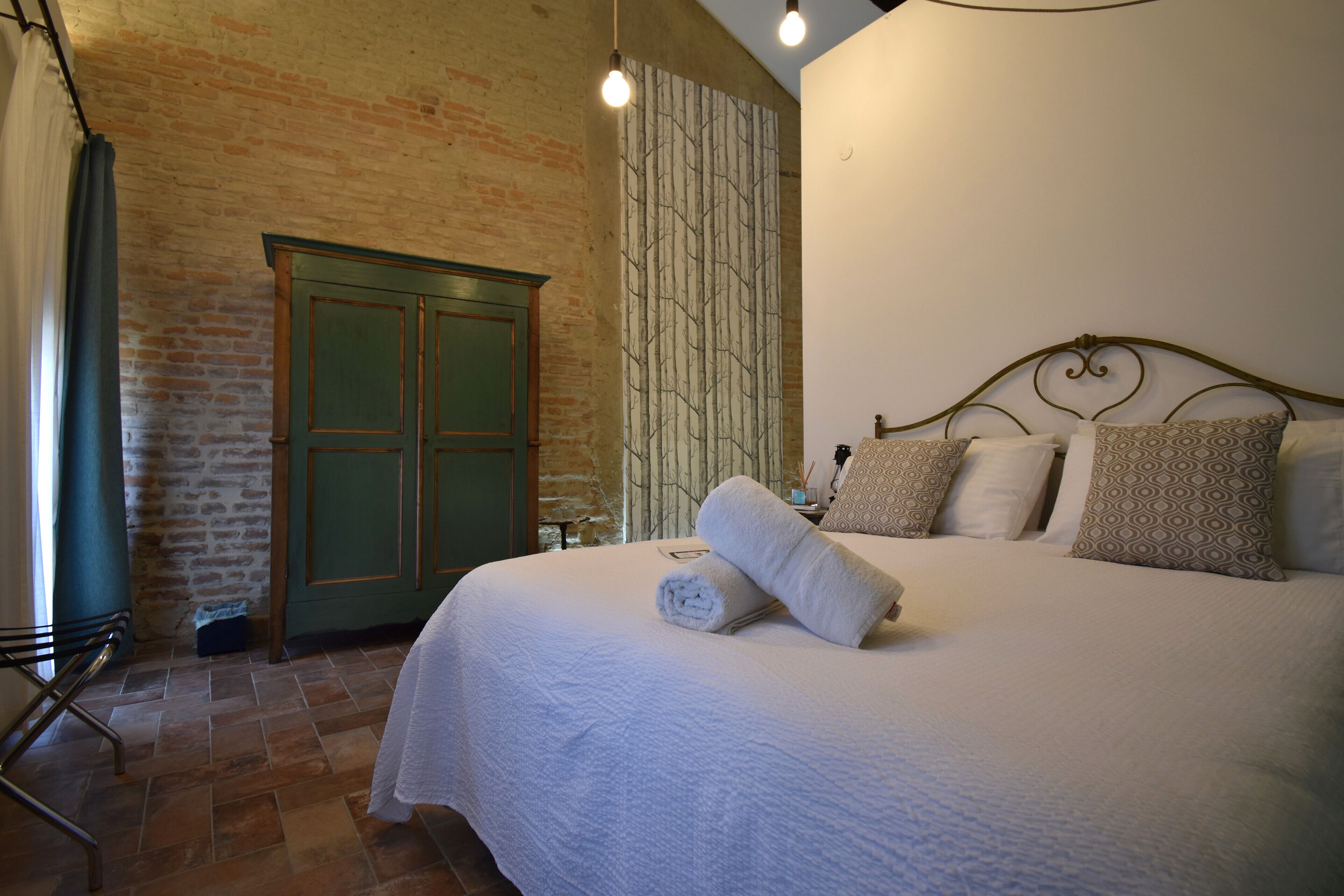 A bedroom with a brick wall, a green door, a bed with white bedding, and a patterned wall.