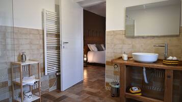 A bathroom with a white sink, mirror, and towel rack. There is a wooden shelf with toiletries and a trash can. The floor is tiled.