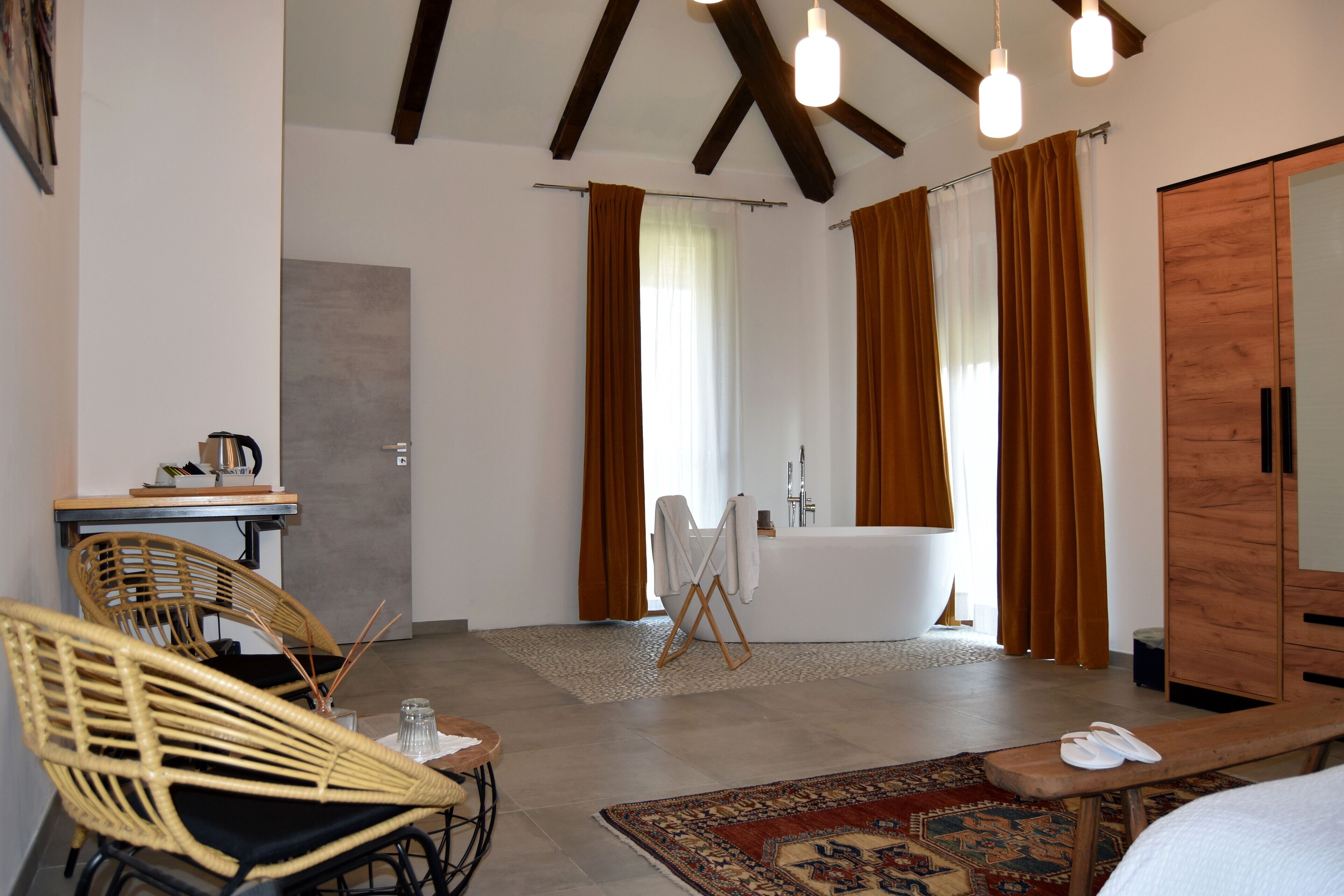 Ein Hotelzimmer mit einem großen Spiegel, einem Holzschrank, einer Sitzecke mit Korbstühlen, einem kleinen Tisch mit Wasserkocher und einem großen Fenster mit Vorhängen.