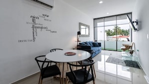 A modern living room with a dining area, featuring a word cloud wall art, a sofa, and a glass table.