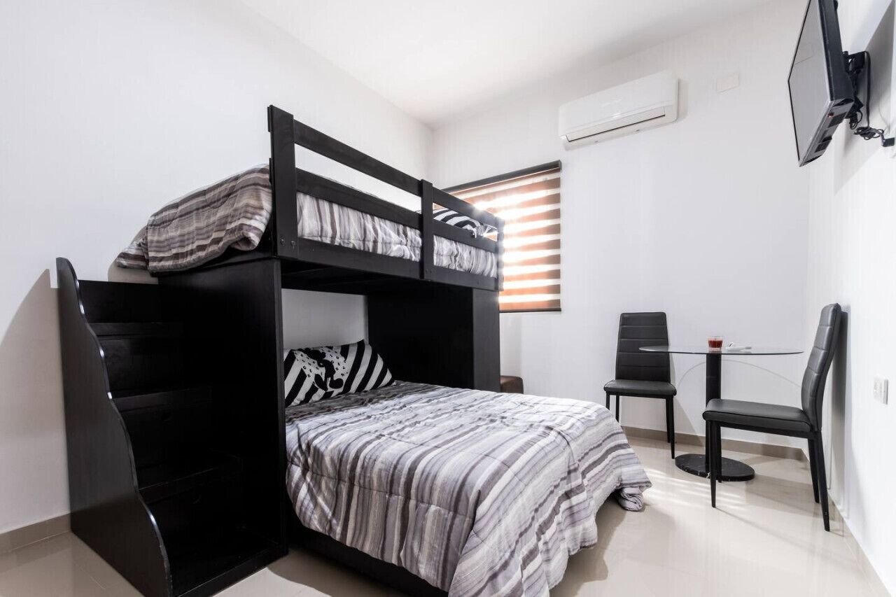 A bunk bed with a striped bedspread, a desk with two chairs, and a window with blinds.