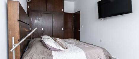 Une chambre moderne avec un lit, une armoire intégrée et un téléviseur fixé au mur.