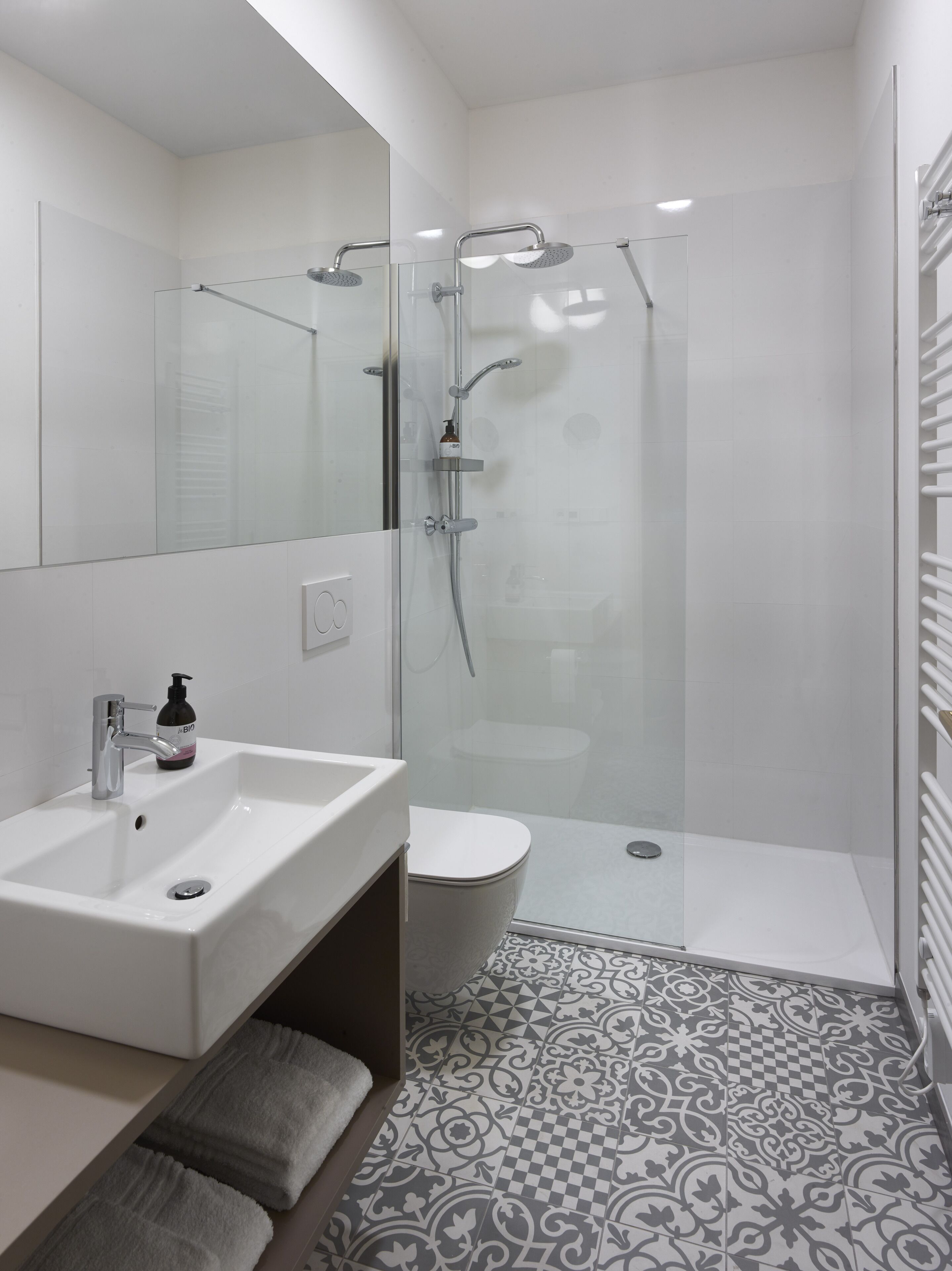 A modern bathroom with a glass-enclosed shower, a white sink, and patterned floor tiles.