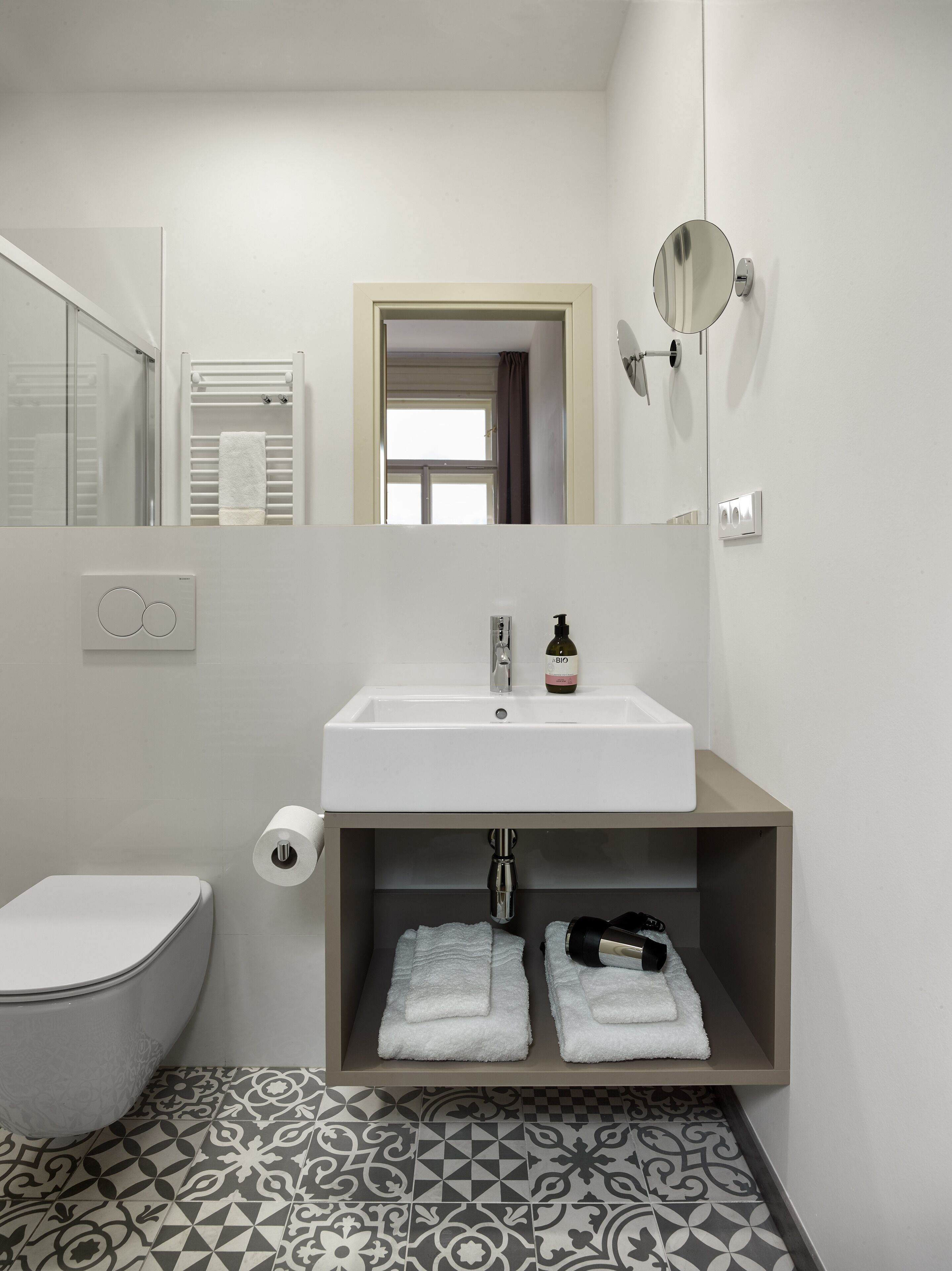Ein modernes Badezimmer mit einem weißen Waschbecken, einer Toilette, Fliesen mit Muster und einem Spiegel mit Wandleuchte.