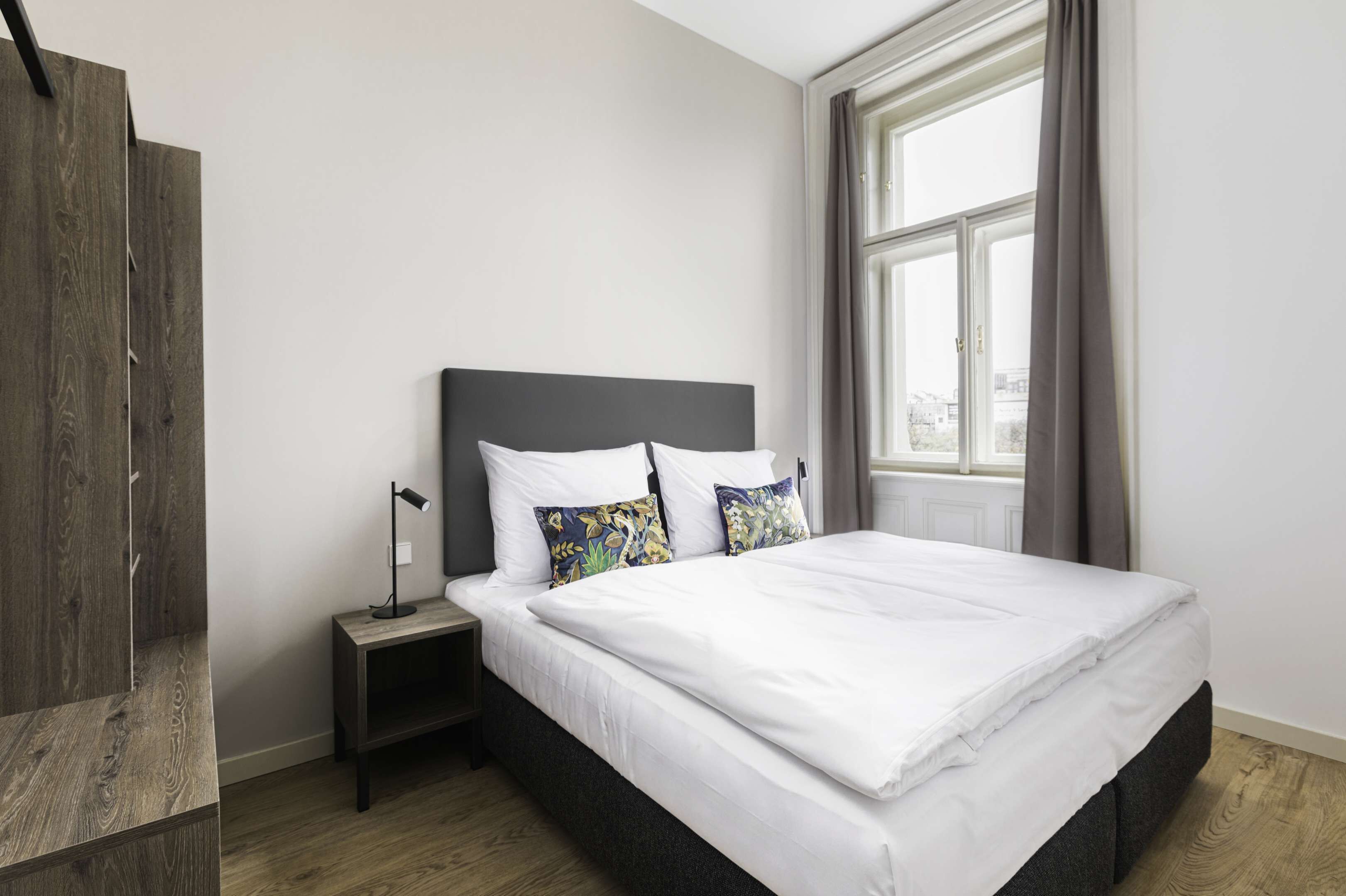 Un lit bien fait, avec du linge de lit blanc, une tête de lit sombre et deux coussins décoratifs.