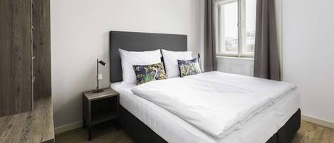 A neatly made bed with white linens, a dark headboard, and two decorative pillows.