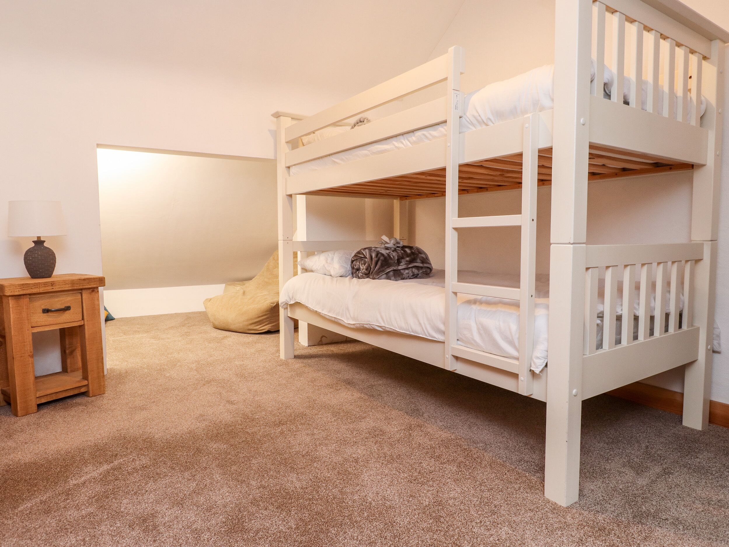 A bunk bed room with a wooden nightstand, a lamp, and a bean bag chair.