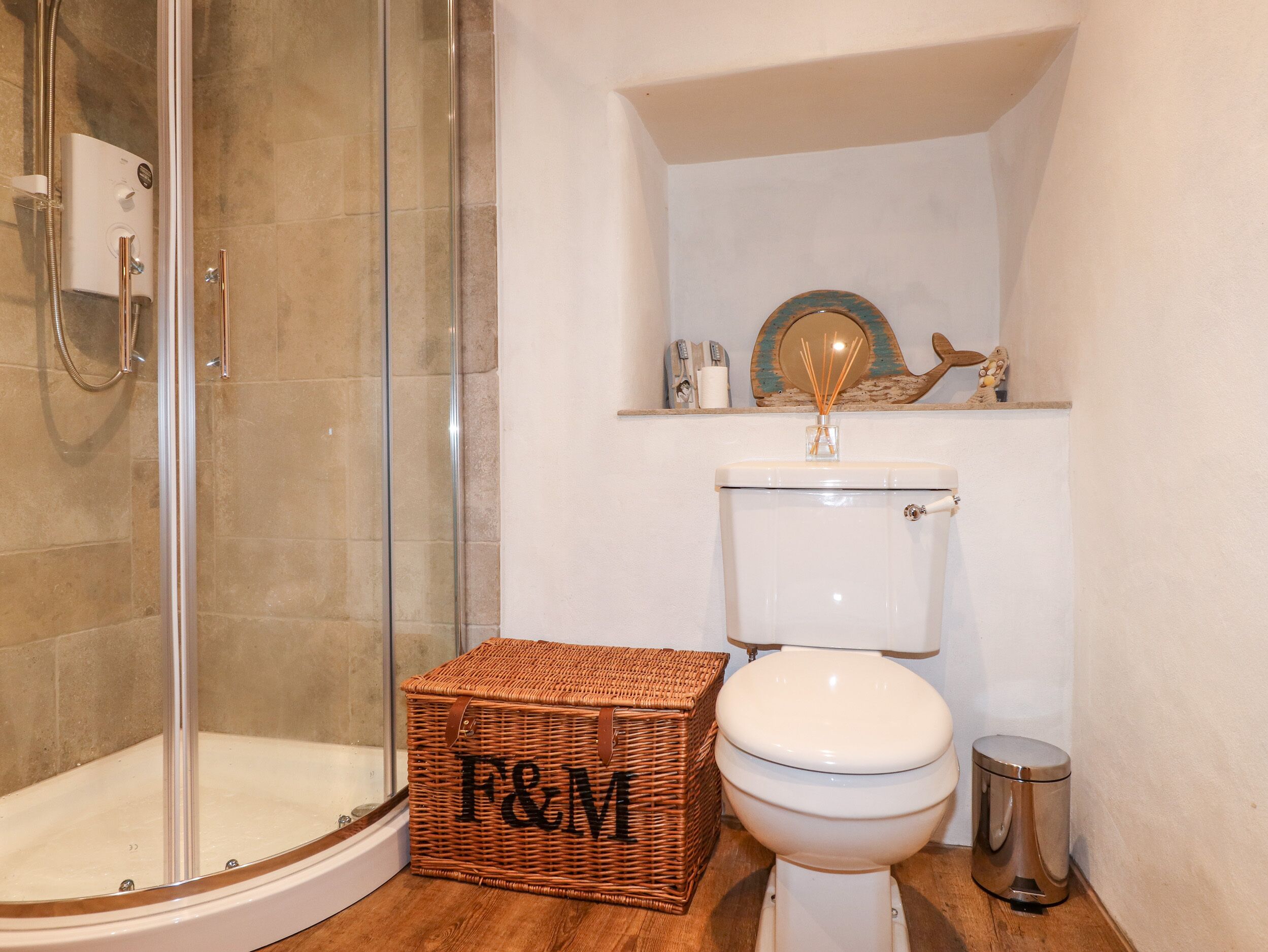 A bathroom with a glass shower enclosure, a white toilet, and a wicker basket with "F&M" on it.