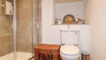 A bathroom with a glass shower enclosure, a white toilet, and a wicker basket with "F&M" on it.