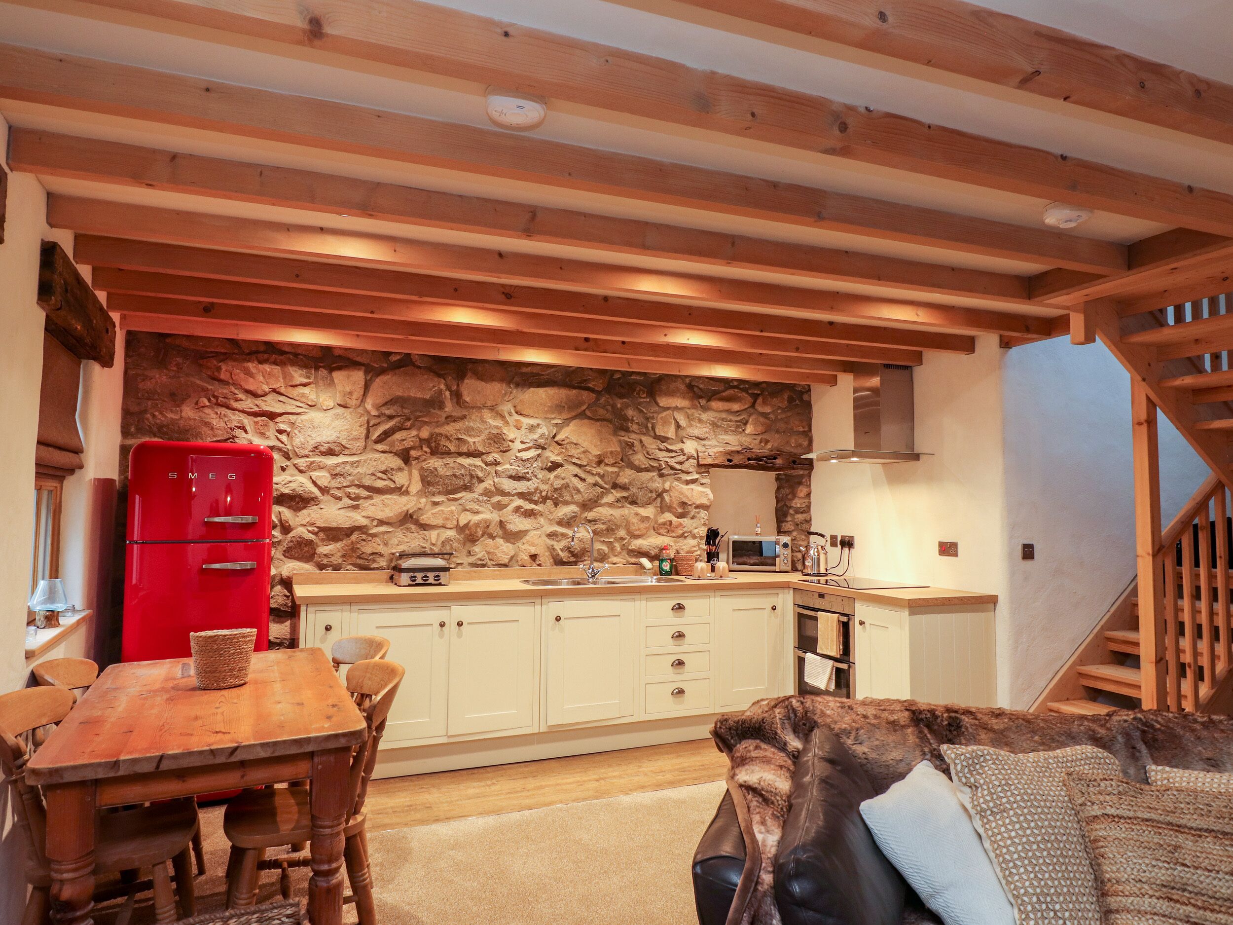 Une cuisine chaleureuse avec un mur en pierre, des poutres en bois, un réfrigérateur rouge et un coin repas comprenant une table et des chaises.