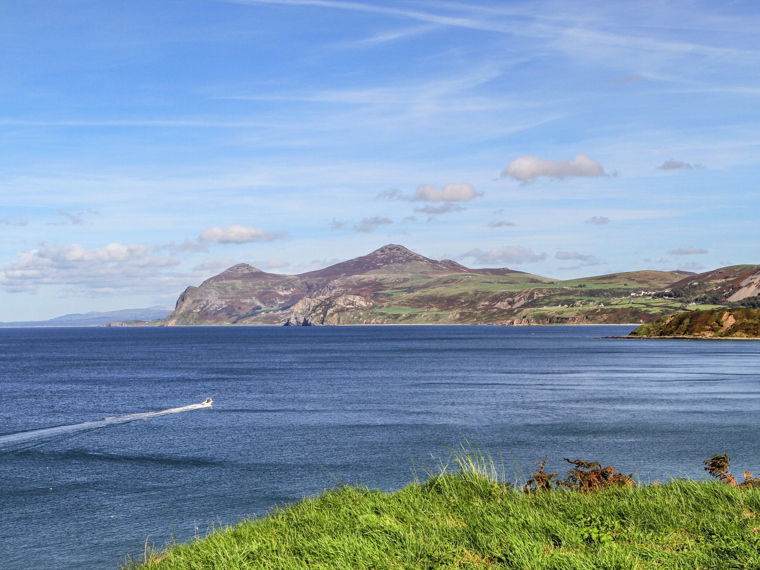 A coastal landscape with a boat on the water, grassy areas, and hills in the background.
