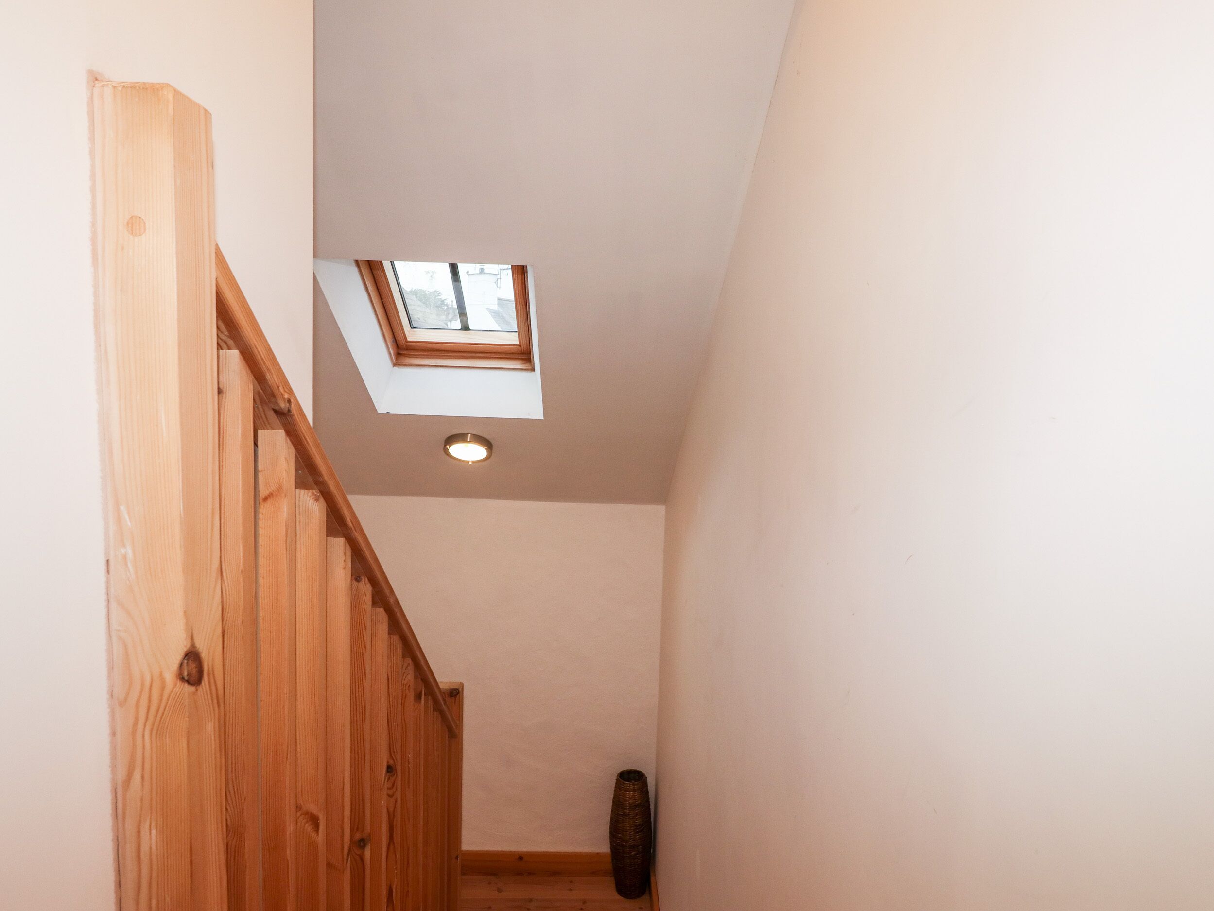 A wooden staircase leading to a loft with a skylight.